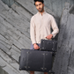 Man holding one black suitcases against a textured gray wall and a small hard shell keepsake 13 inch minimalist structured design